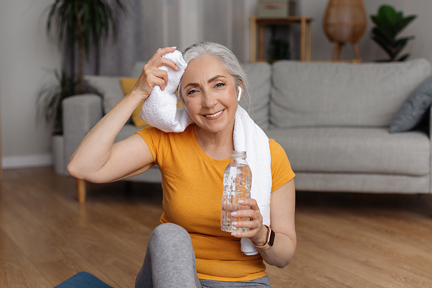 Happy senior woman with bottle of water wiping sweat